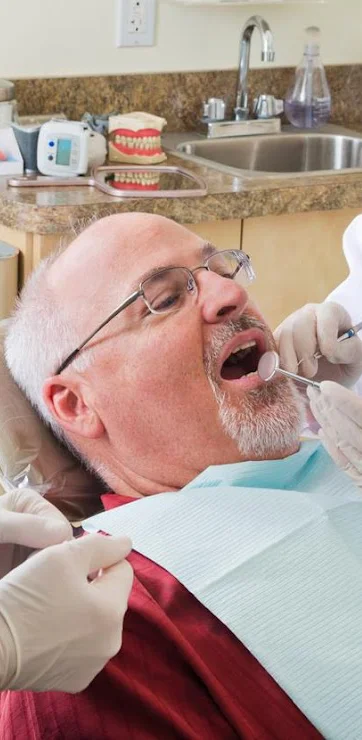 A man lying in a dental exam chair while a dentist examines his teeth